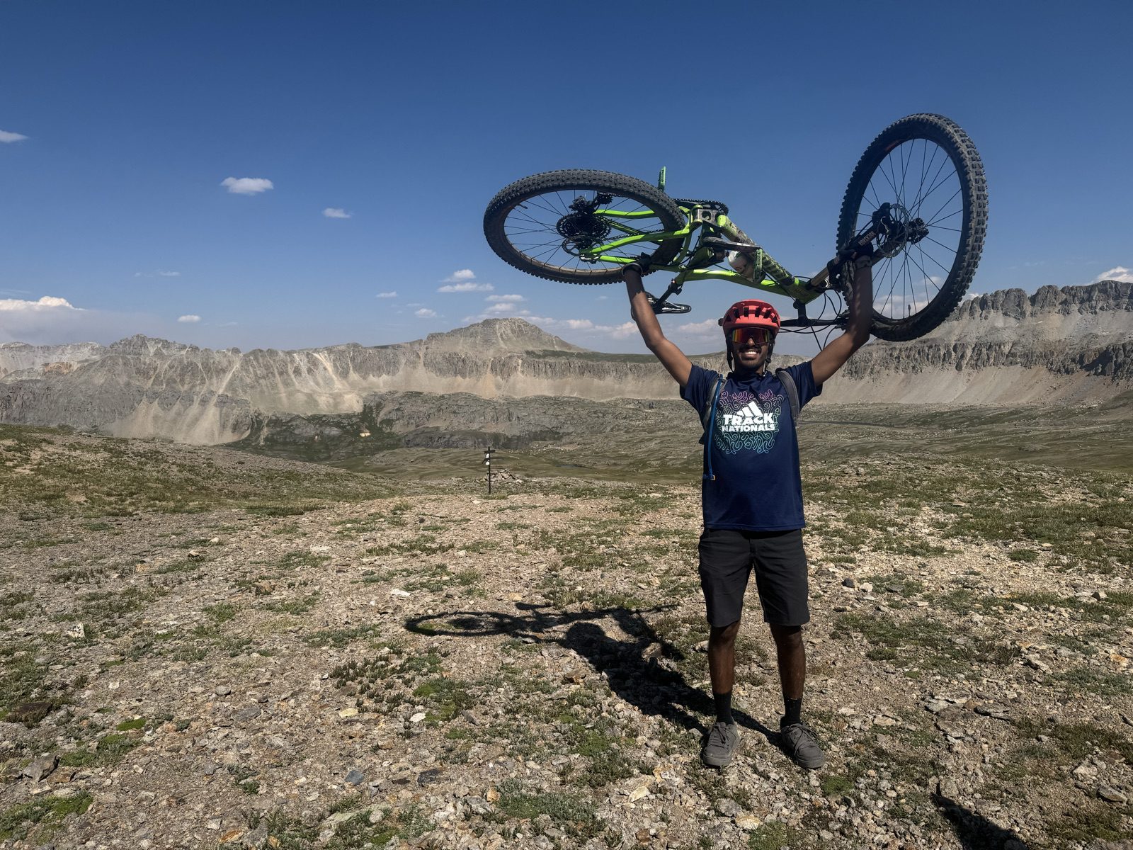 Mountain biker holding bike overhead at a 13,073-foot saddle in the San Juan Mountains