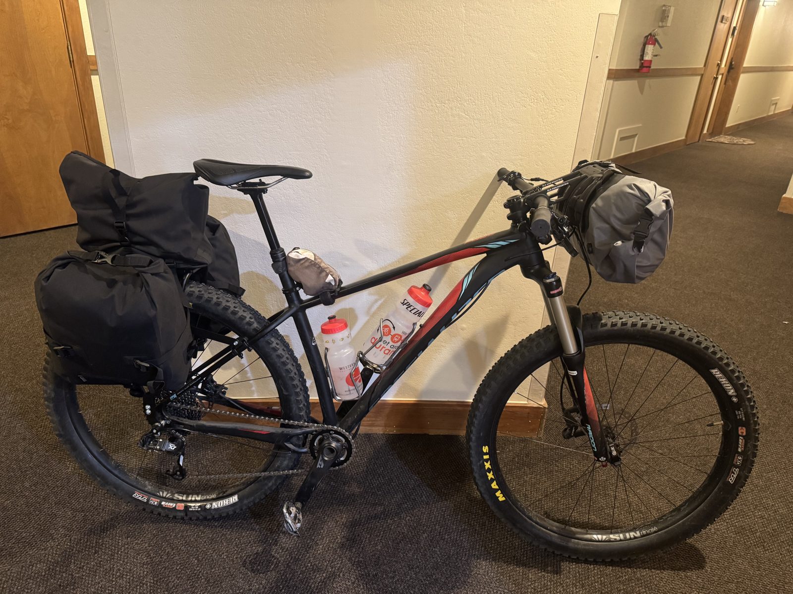 Loaded Specialized Fuse hardtail with rear rack, trunk bag, and handlebar cradle the night before a bikepacking trip