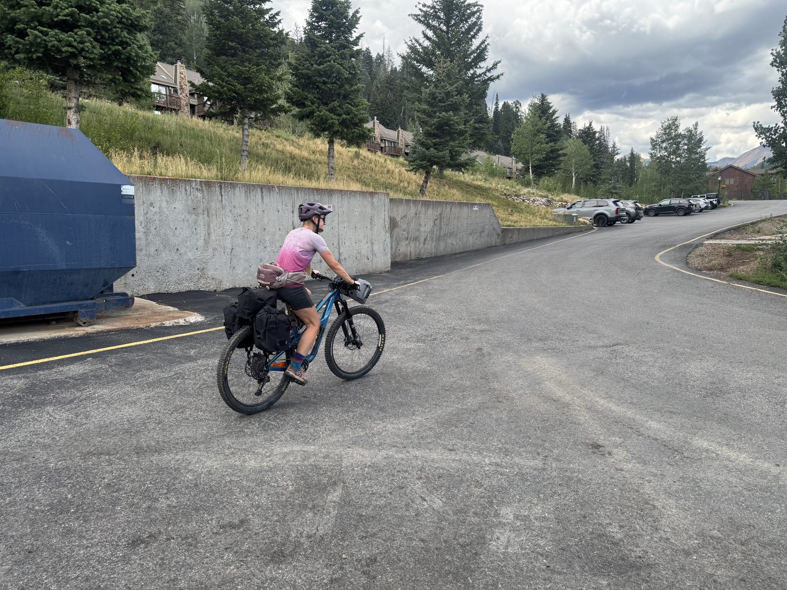 Cyclist with loaded bikepacking bike at Purgatory Resort parking area under dark storm clouds