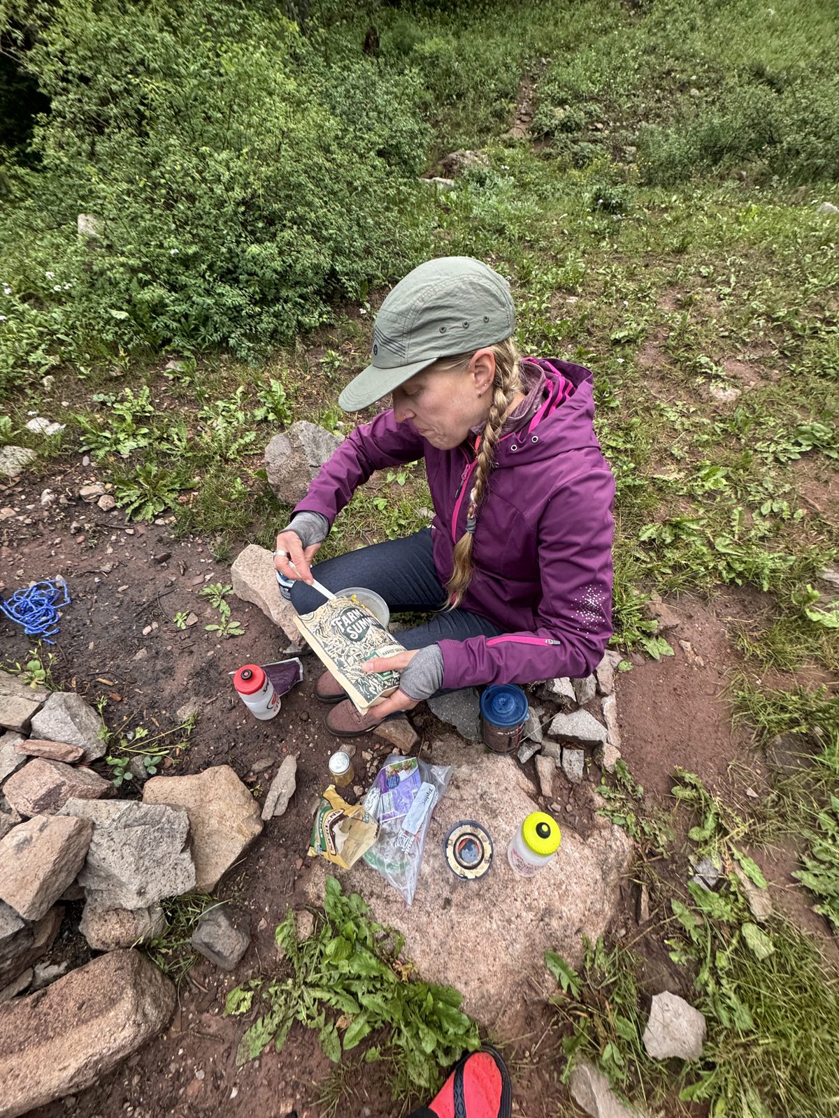 Camper sitting at a rock eating a Farm to Summit dehydrated meal at a forest campsite