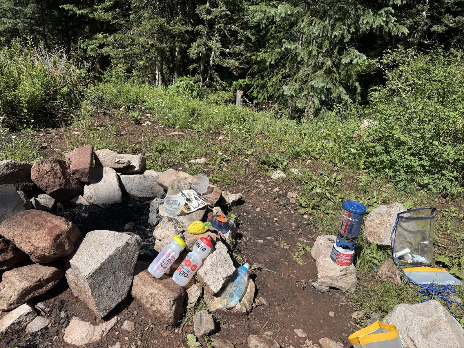 Backcountry camp kitchen with a fire ring, camp stove, and gear laid out on rocks
