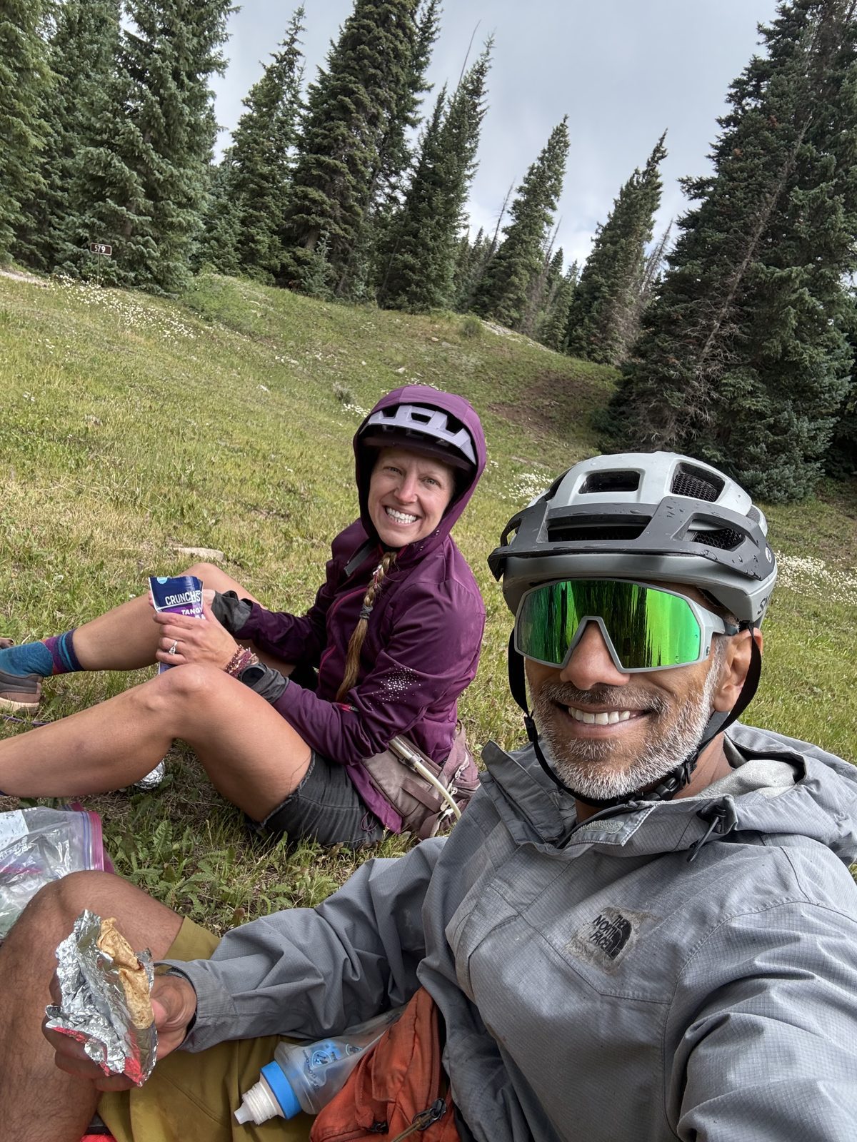 Selfie of two smiling cyclists in helmets taking a snack break on a bikepacking trip